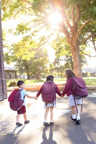 Three school children, holding hands, walking through playground