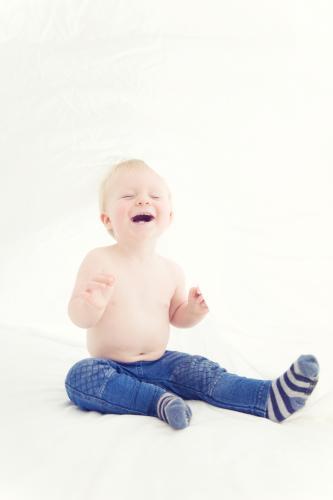 Toddler sitting on bed under the sheets wearing jeans and socks laughing