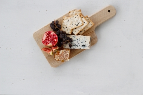 Top down view of wooden cheese board with cheese, crackers, pomegranate, figs and muscatels