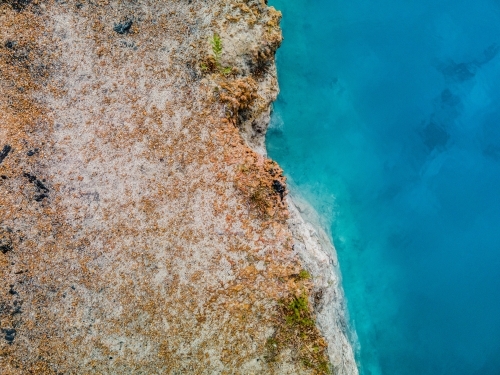 top view shot of a blue water meeting with a brown and white rock formation