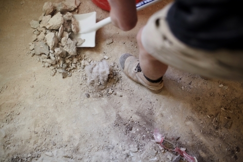Tradesman shovelling debris off a dirty floor in a construction site