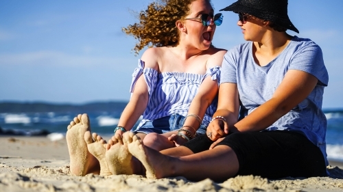 Two girls sitting on beach with sandy feet