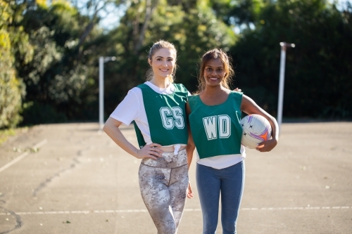 Two women standing in a court wearing sportswear while one was holding a ball