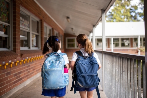 Two young schoolgirls walking along outdoor hallway
