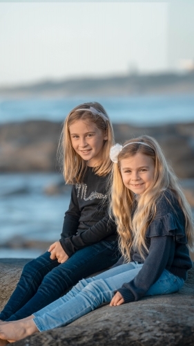Under 10 girls sitting on rock at beach