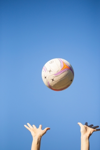 vertical shot of a ball thrown up in the air by two hands with clear skies in the background