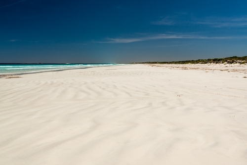 Wave patterns on a white sand beach leading to a far horizon and dark polarised blue sky