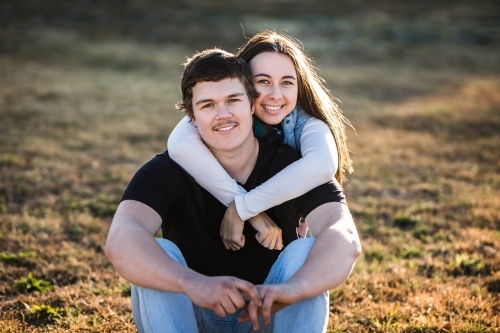 Woman sitting behind boyfriend with arms wrapped around him smiling