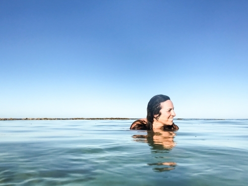 Woman submerged and floating in calm ocean on clear day