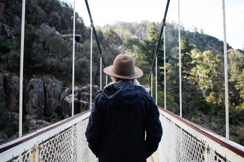 Woman wearing hat and jacket looking out over suspension bridge