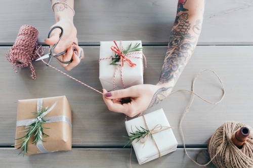 Woman with sleeve tattoo cutting twine while wrapping gifts