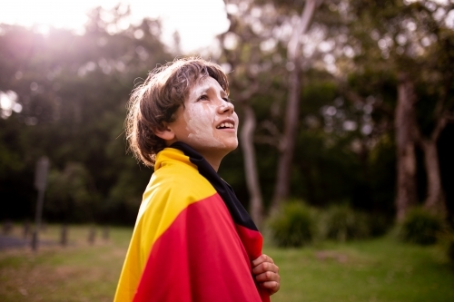 Young Aboriginal boy wearing Aboriginal flag around his shoulders and looking up