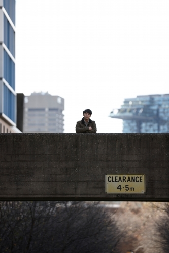 Young Asian man standing on bridge with city in background