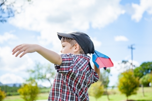 Young boy flying a paper plane outside
