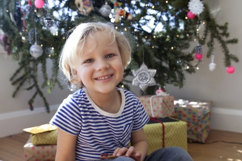 Young boy sitting in front of Christmas tree looking and smiling at camera
