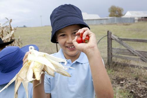 Young boy wearing school uniform holding up freshly picked vegetables