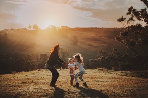 Young children playing with their mother in a field at sunset