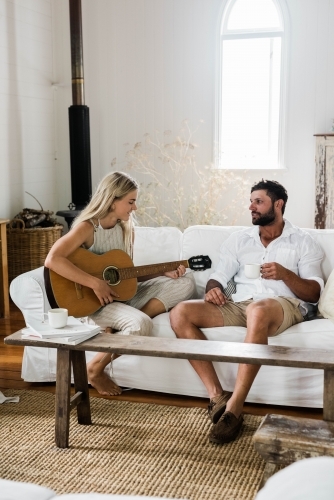 Young couple sitting on a couch, with the woman playing guitar.