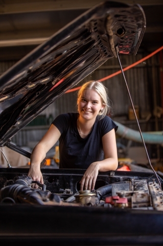young female australian tradesperson mechanic working on car engine in auto repair garage