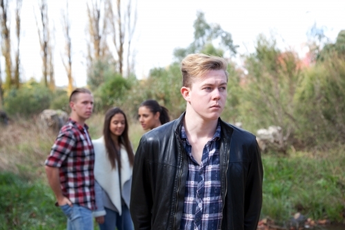 Young male standing in front of a group of young people talking in an outdoor setting