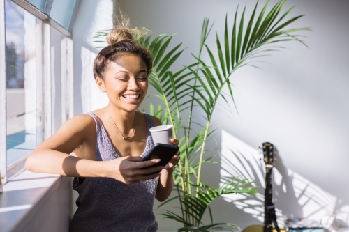 Young woman laughing while having coffee and looking at her phone