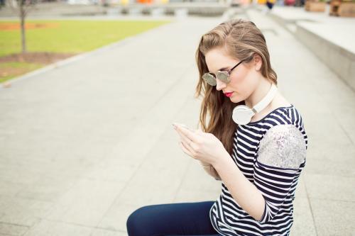 Young woman looking at phone wearing sunglasses and headphones