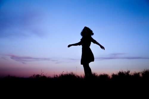 Young woman twirling silhouetted against pastel dusk sky