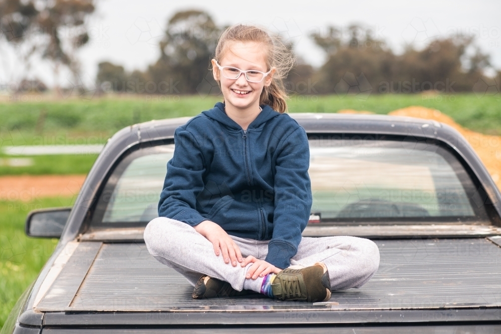 10 year old girl sitting on the back of an old car. - Australian Stock Image