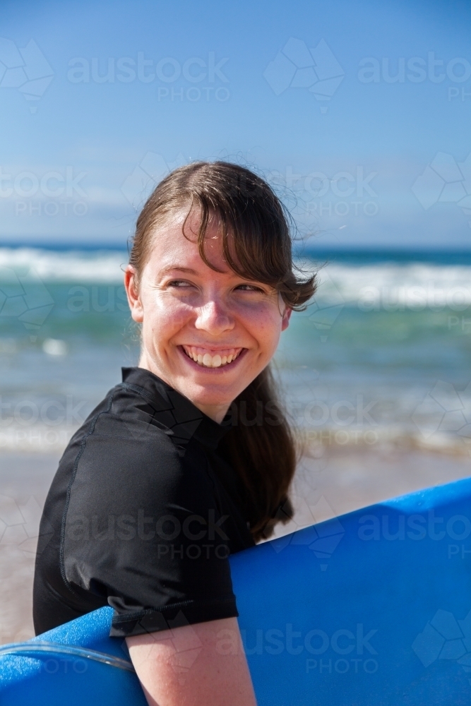 16 year old girl carrying a surfboard down the beach to the ocean - Australian Stock Image