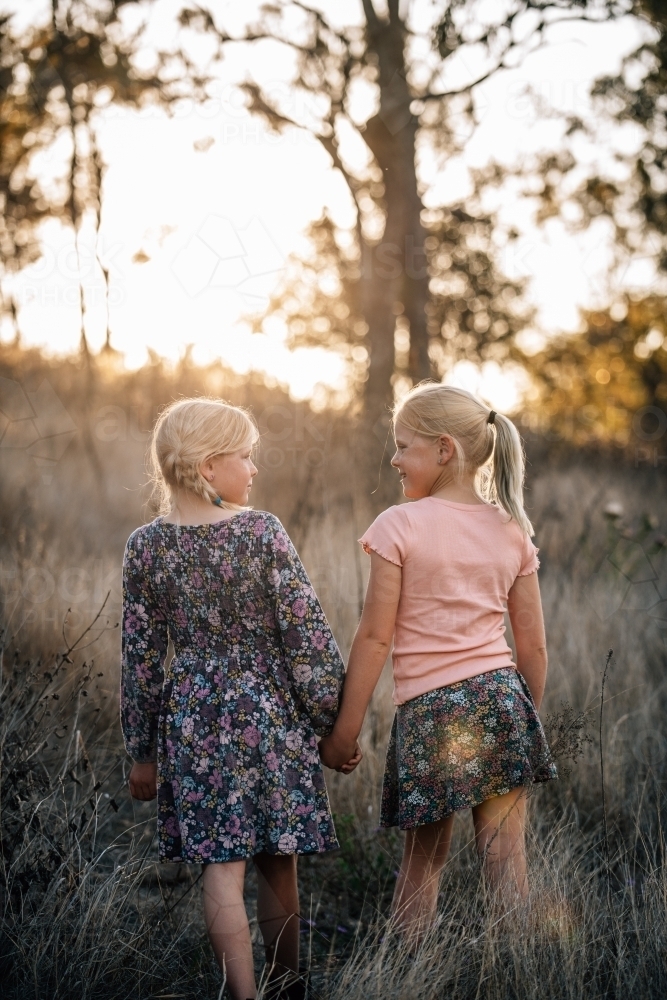 2 young girls holding hands looking at each other as they walk away - Australian Stock Image