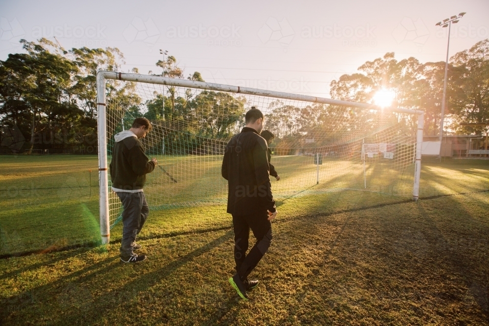 3 men walking on the field near the soccer net during sun set - Australian Stock Image