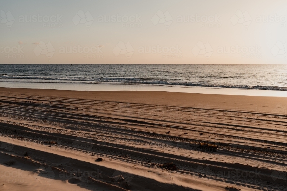 4WD tyre tracks on the beach and a calm ocean at sunset - Australian Stock Image