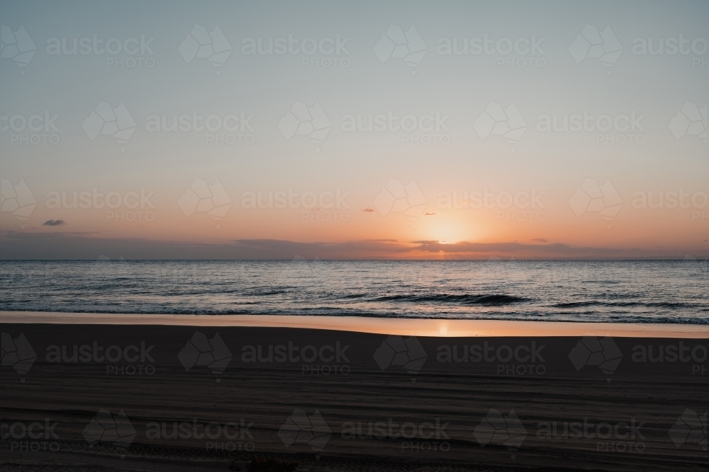 4wd tyre tracks on the beach and a calm ocean at sunset - Australian Stock Image