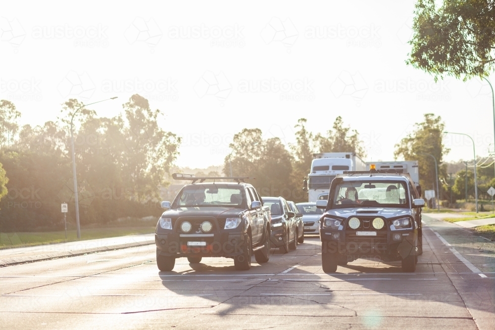 4x4 car and ute stopped at traffic light intersection backlit by sunlight - Australian Stock Image