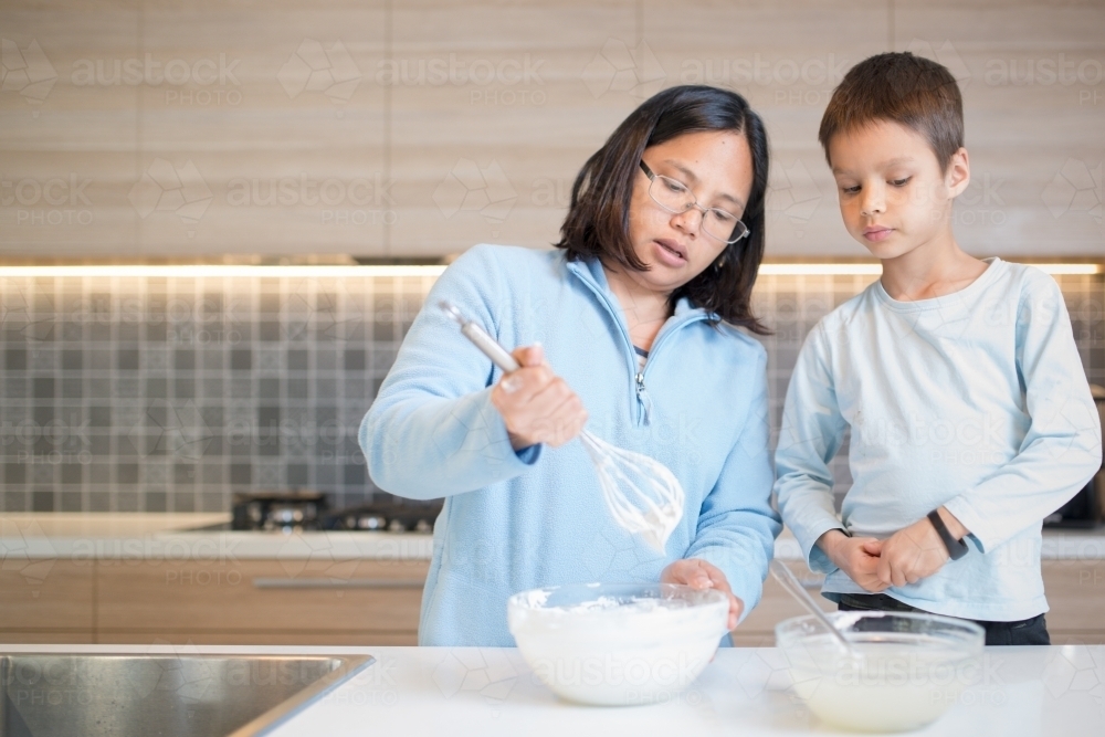 7 year old mixed race boy cooks at home with a whisk and bowl - Australian Stock Image