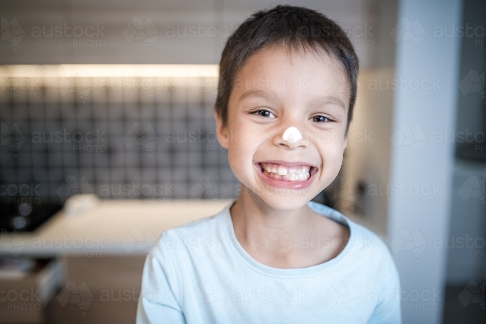 7 year old mixed race boy laughs at the mess he's made on his face while cooking at home - Australian Stock Image