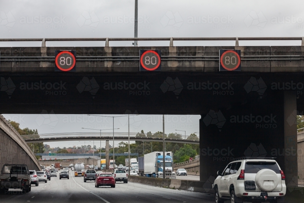 80 speed sign on overhead bridge with busy road through city - Australian Stock Image