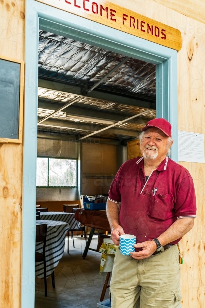 A bearded man standing in a dooway holding a coffee mug in a Men's shed - Australian Stock Image