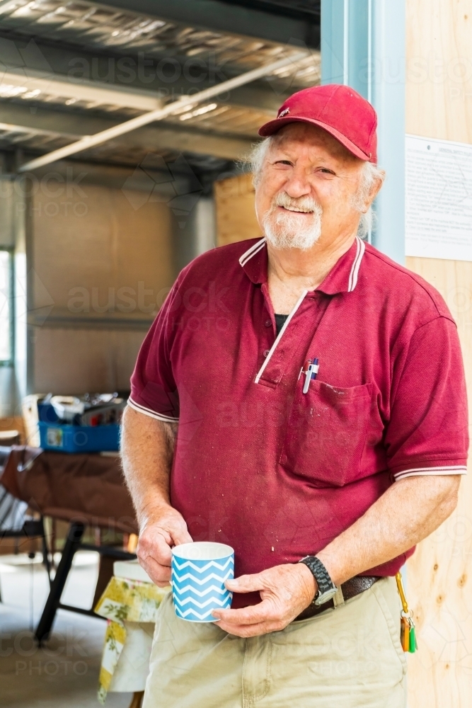 A bearded man standing in a dooway holding a coffee mug in a Men's shed - Australian Stock Image