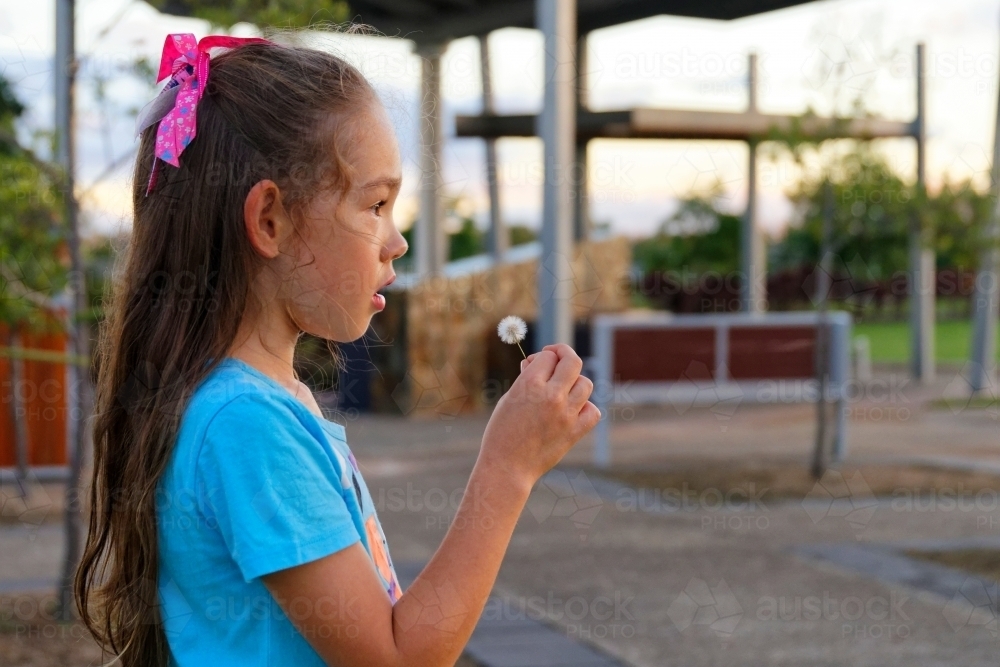 A Beautiful young girl at sunset blowing a dandelion flower to make a wish close up - Australian Stock Image