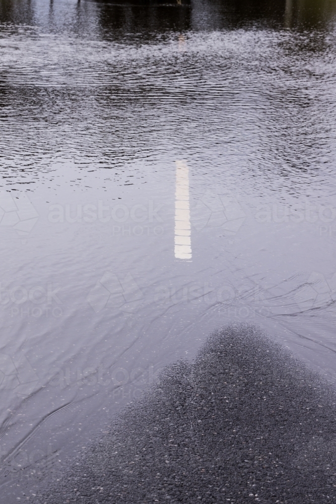 A bitumen road dangerously disappears under flood water from a storm - Australian Stock Image