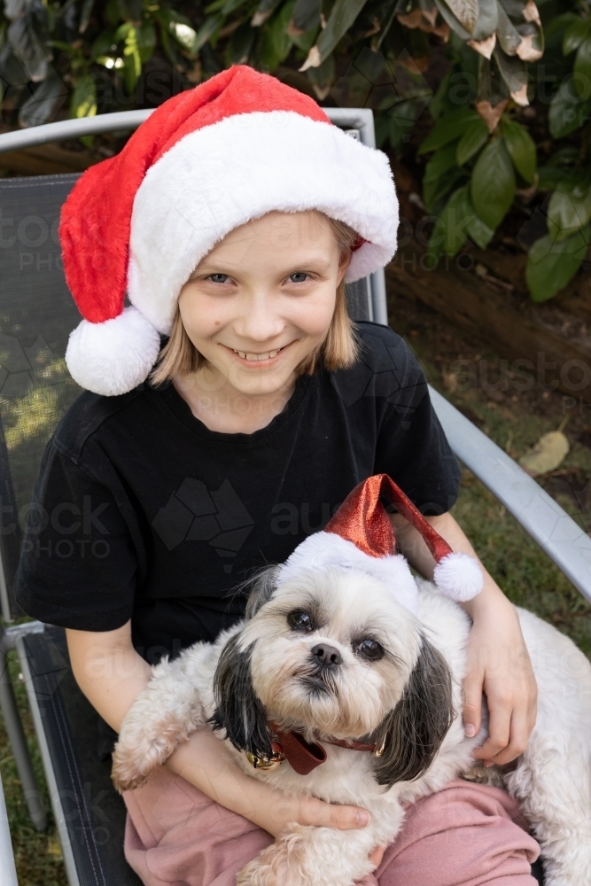 A blonde caucasian australian girl wearing a Santa had while holding her pure bred dog - Australian Stock Image