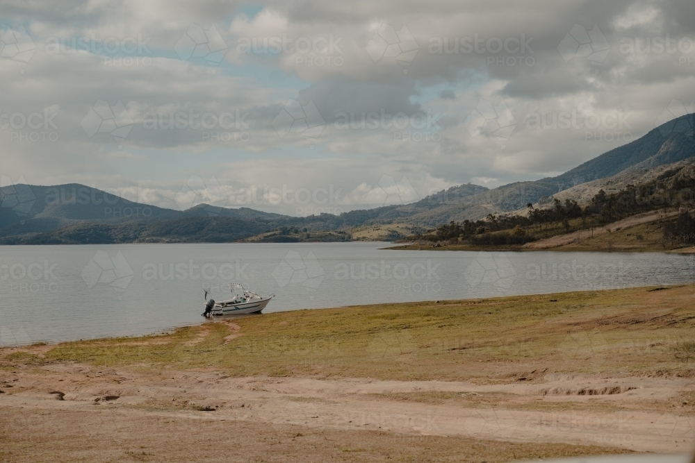 A boat at the edge of a lake with mountains in the background - Australian Stock Image