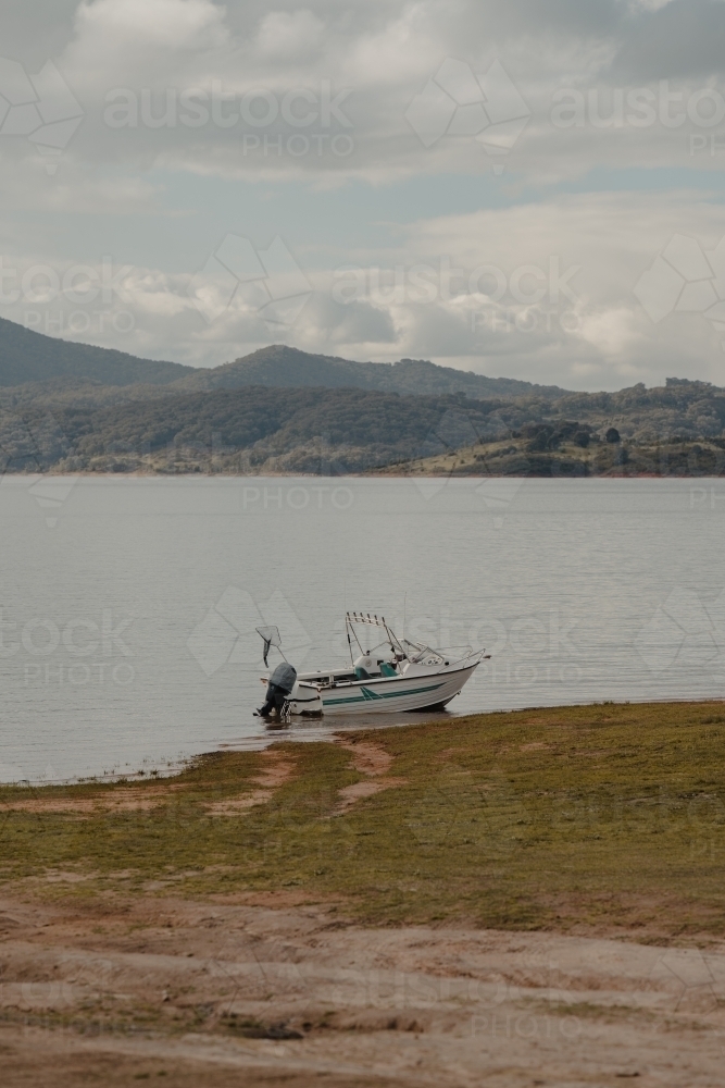 A boat at the edge of a lake with mountains in the background - Australian Stock Image