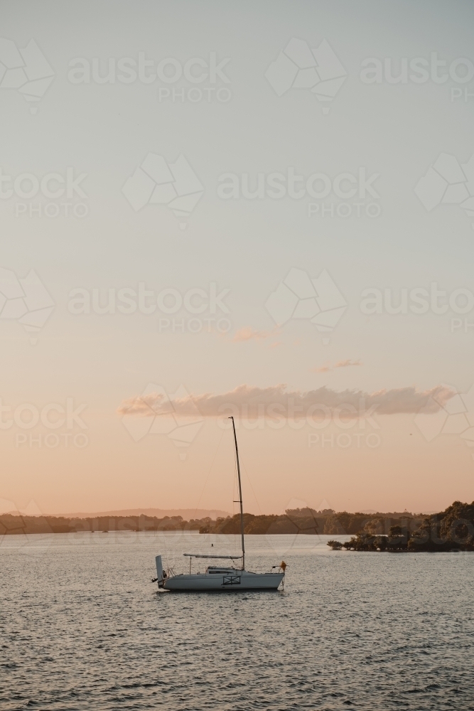 A boat sitting on the calm river at sunset near the Yamba Marina on the Clarence River. - Australian Stock Image