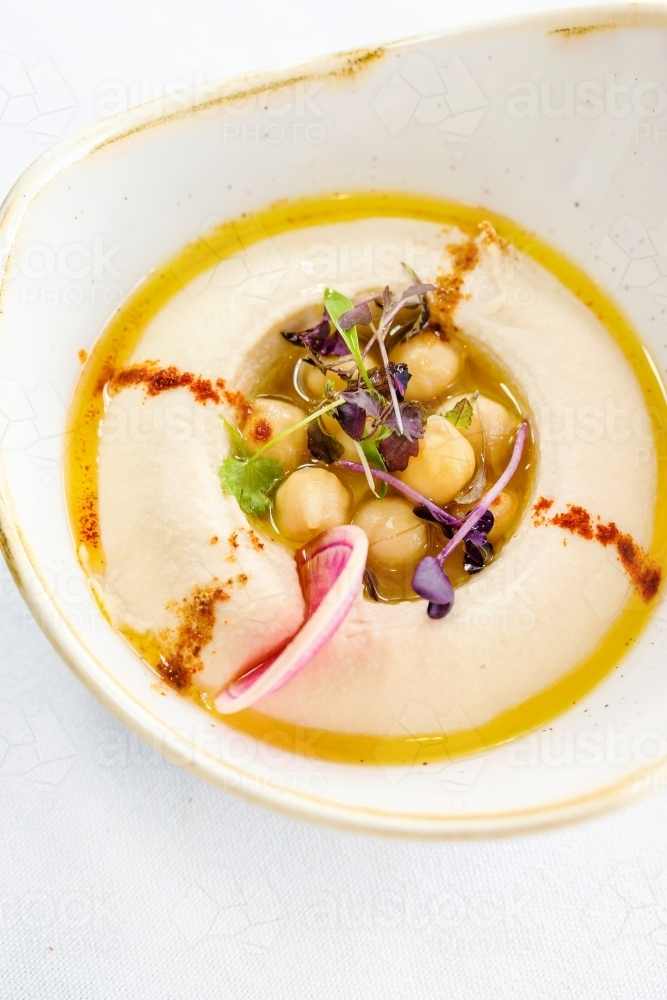 A bowl of hummus topped with chickpeas, herbs, and olive oil. - Australian Stock Image