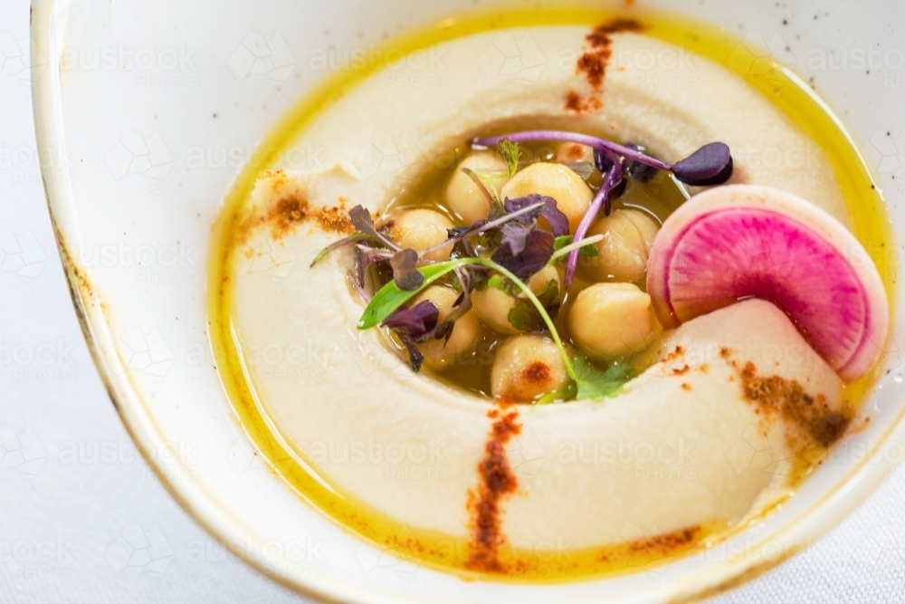 A bowl of hummus topped with chickpeas, herbs, and olive oil. - Australian Stock Image