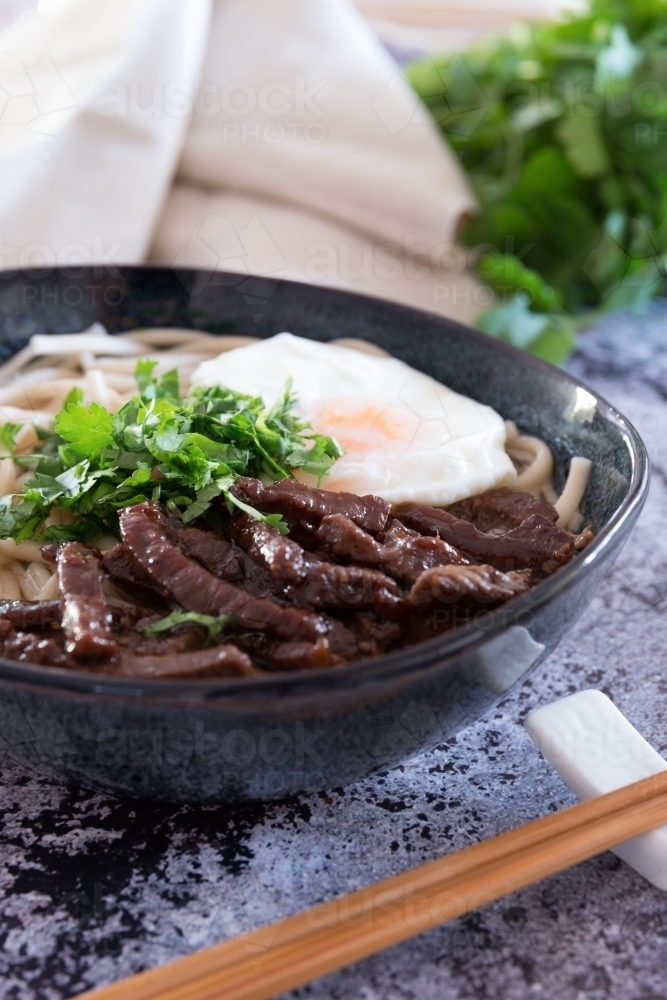 A bowl of wagyu noodle soup topped with sunny side up egg and beef slices - Australian Stock Image