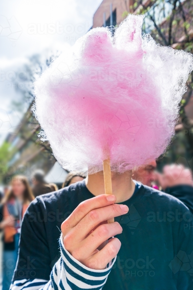 A boy holding a stick of fairy floss in front of his face - Australian Stock Image