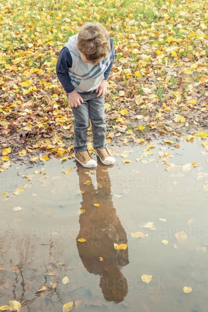 A boy looking at his reflection in a large puddle - Australian Stock Image